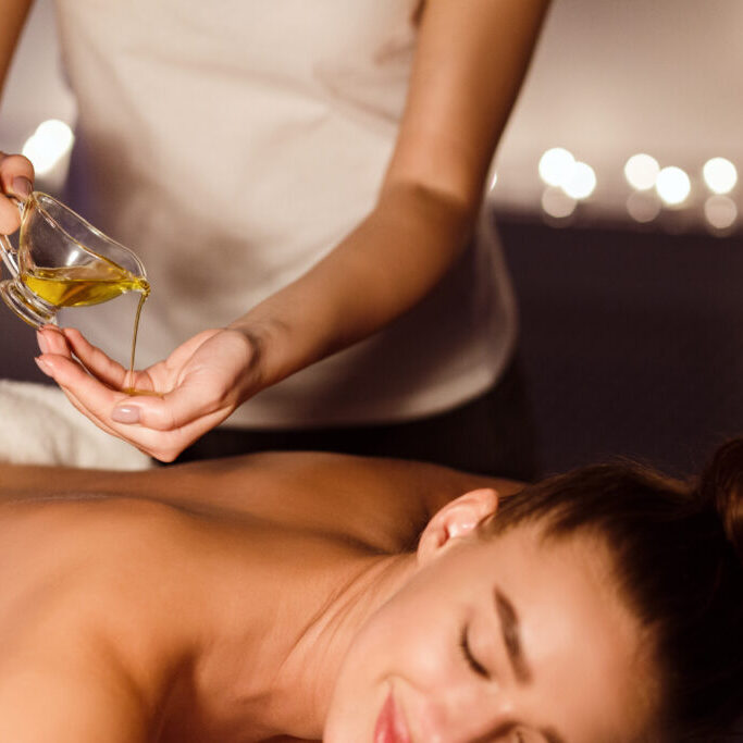 Relaxing treatment. Masseur pouring aroma oil on hand, preparing for massage